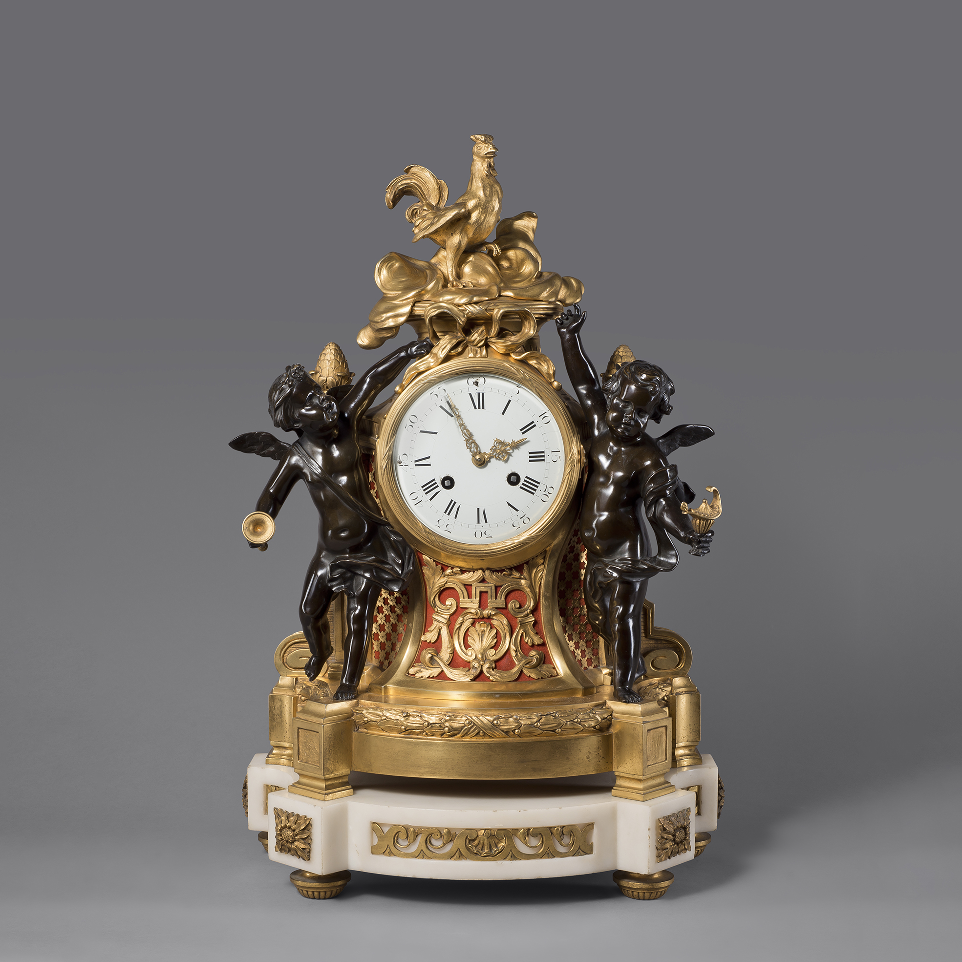 Louis XVI style gilt and patinated bronze figural clock with bacchic cherubs, cockerel finial, and white marble base, France, circa 1870.
