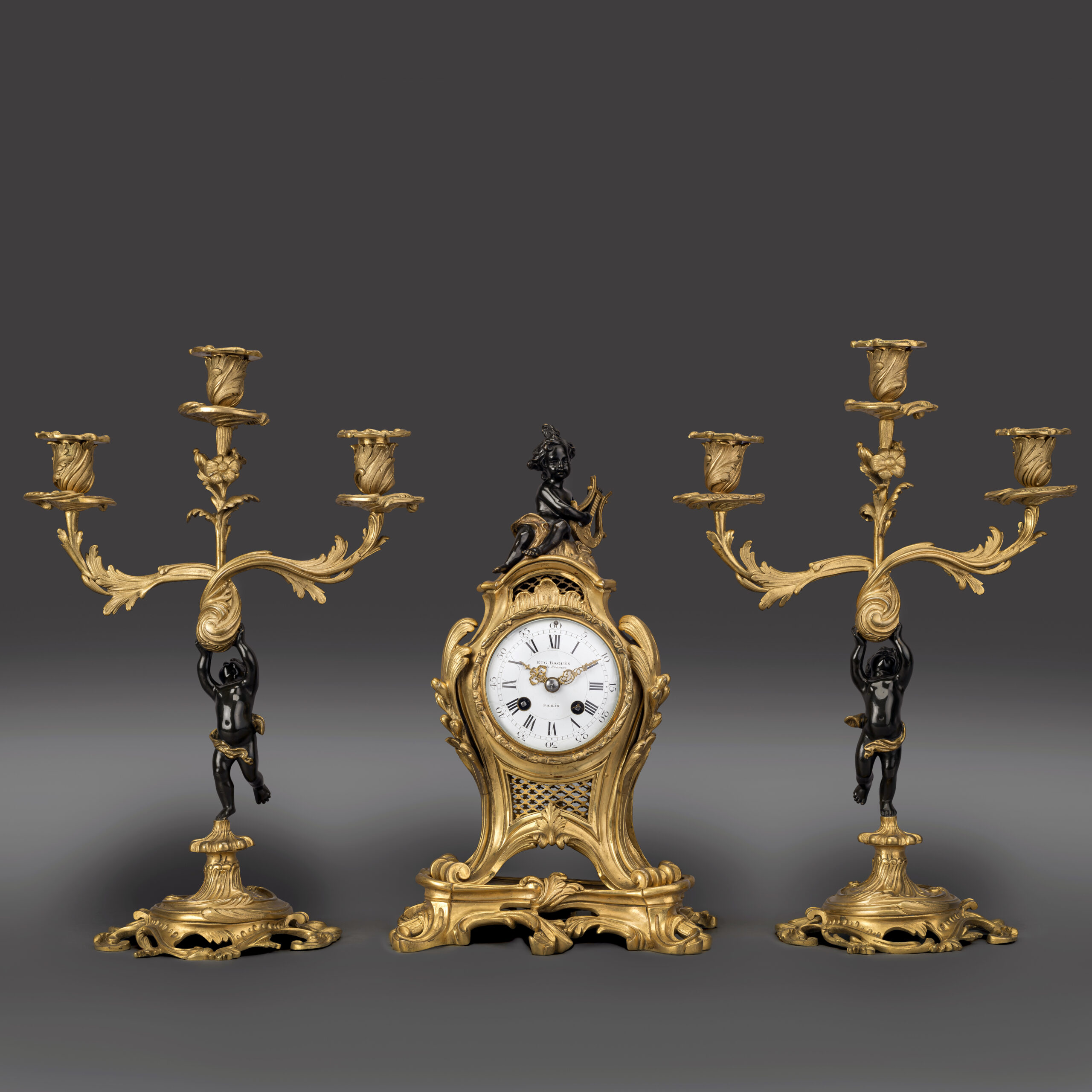 Louis XV style gilt and patinated bronze clock garniture by Maison Baguès, Paris, comprising a figural clock with putto and matching candelabra, circa 1870.
