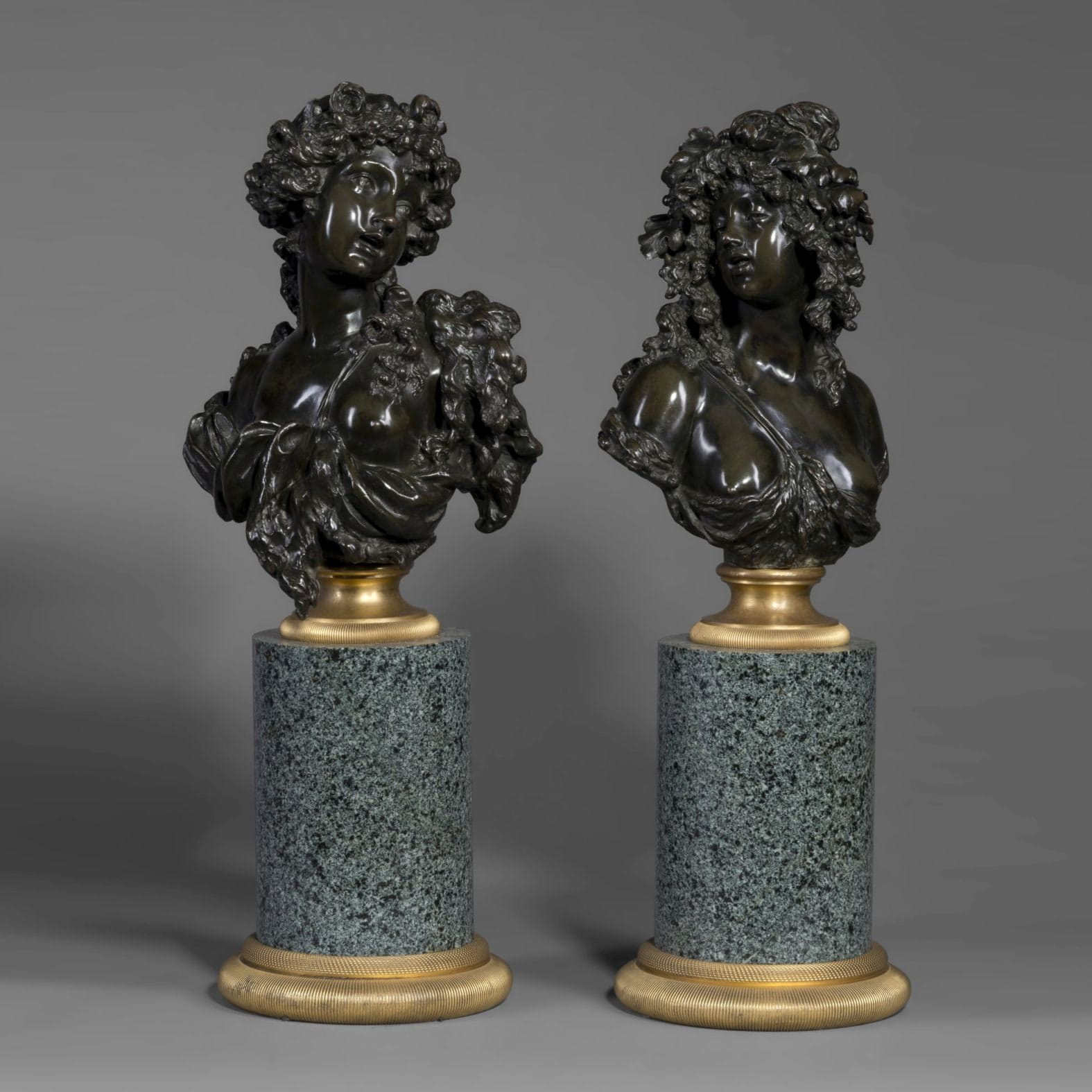 Pair of patinated bronze busts of Bacchantes, one with roses symbolizing Summer and the other with oak leaves for Autumn, after Marin, on gilt-bronze socles and granite plinths, French circa 1890.