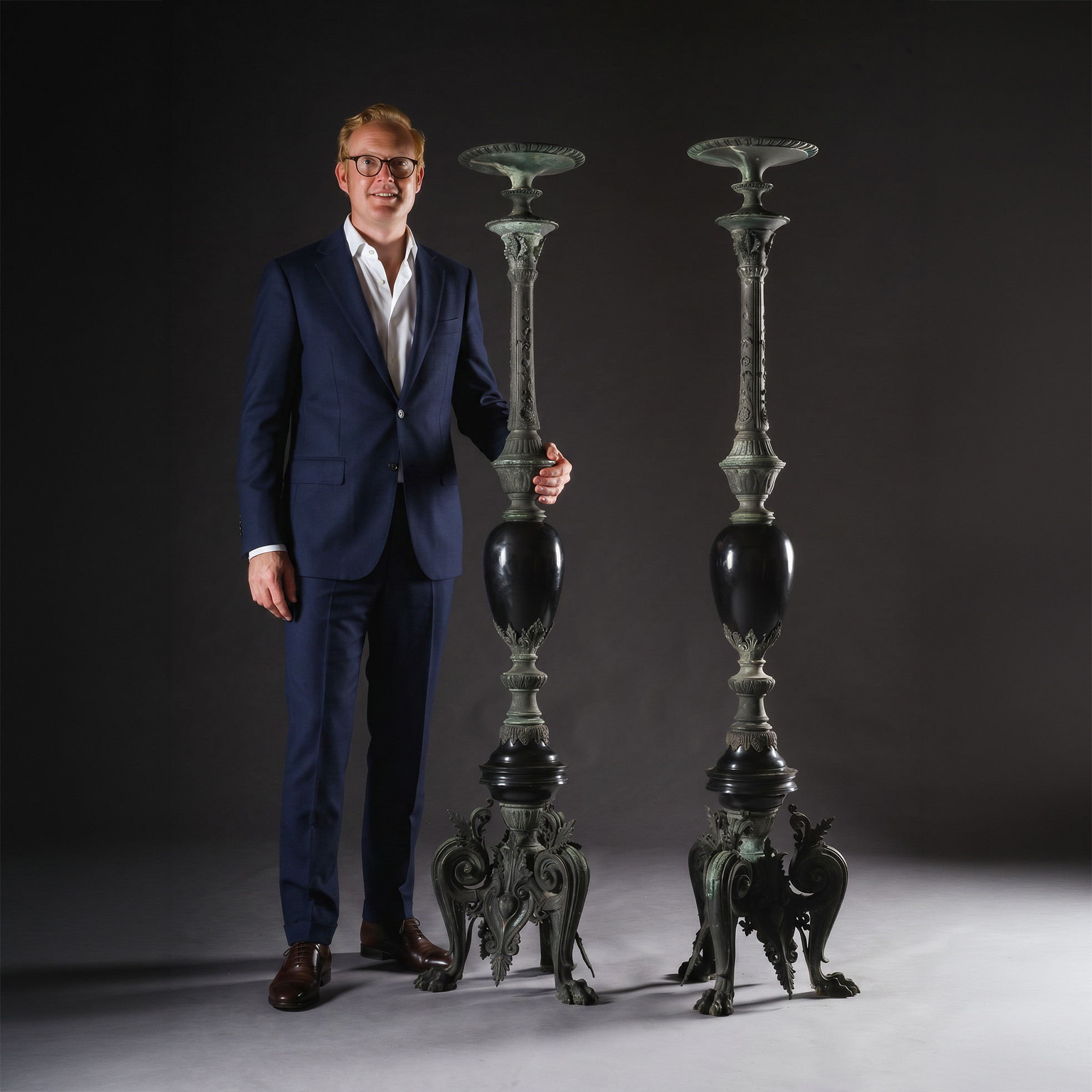 Giles Forster of Adrian Alan Ltd standing next to a fine pair Of Napoleon III Period ‘Neo-Grec’ Bronze And Black Marble Torchères