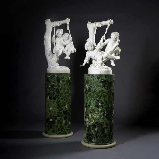 Pair of Carrara marble figural groups of children on swings by Alessandro Lazzerini, Italy, circa 1900, displayed on green scagliola pedestals.