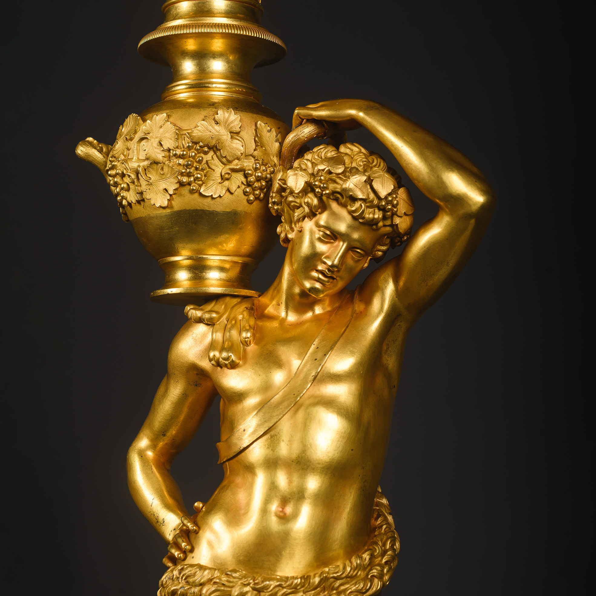 Detail of the gilt-bronze male figure draped in a lion pelt, referencing Hercules, with raised arms supporting an ornamental amphora.